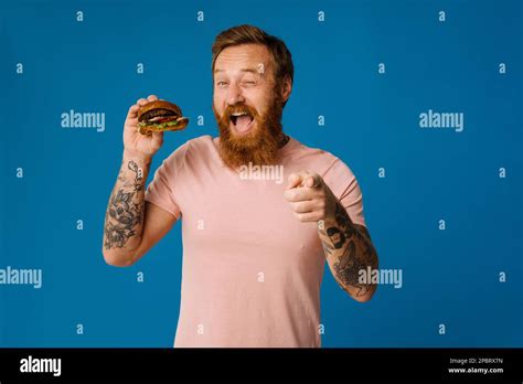 White Hungry Bearded Man Eating Burger Isolated On Blue Background