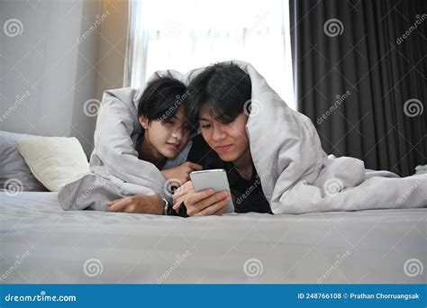 Jovem Casal Gay Deitado Debaixo De Cobertor Na Cama E Usando Um Telefone Inteligente Juntos