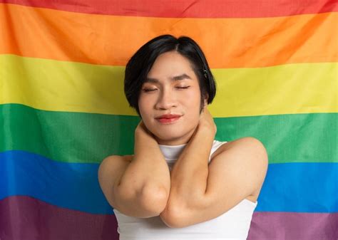 Imagen de un hombre gay asiático sosteniendo una bandera arcoíris posando con confianza sobre un