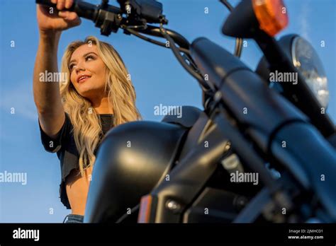 A Lovely Blonde Model Enjoys The Outdoor Weather While Posing With Her Motorcycle Stock Photo