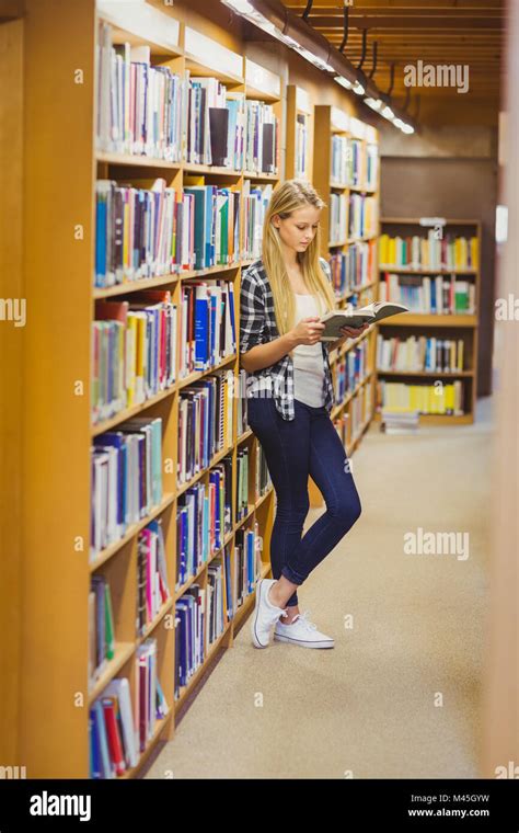 Blonde Student Reading Book Next To Bookshelf Stock Photo Alamy