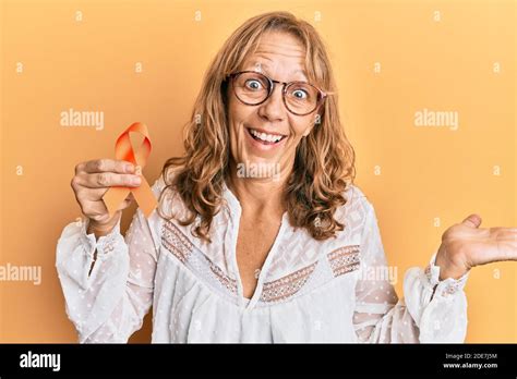 Middle Age Blonde Woman Holding Awareness Orange Ribbon Celebrating Achievement With Happy Smile