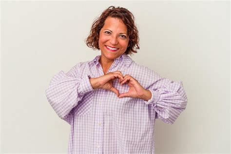 Mulher latina de meia idade isolada no fundo branco sorrindo e mostrando uma forma de coração