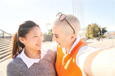 Selfie Of An Interracial Lesbian Happy Couple Smiling Asian Woman And A Cheerful Caucasian Girl