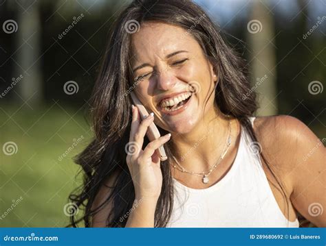 Woman Laughing While Talking On The Phone Standing Outdoors In Nature