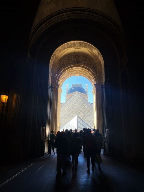 People Are Walking Under An Arch In The City At Night With Light Coming