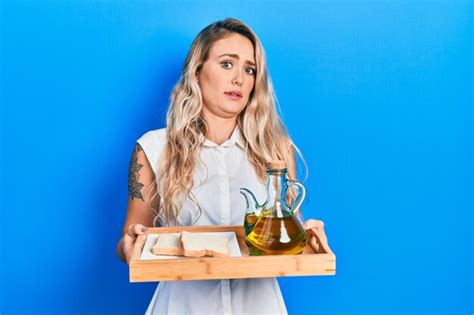 Schöne junge blonde Frau hält ein Tablett mit Olivenöl und Brottoast in der Hand ahnungsloser