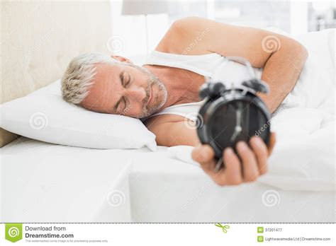 Sleepy Mature Man Holding Alarm Clock In Bed Stock Image Image Of