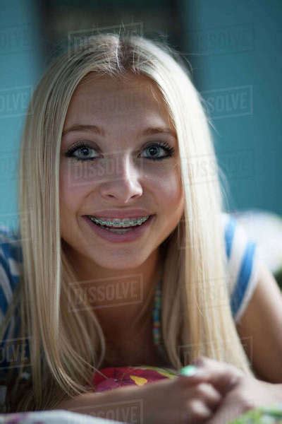 Close Up Of Smiling Teenage Girl With Long Blonde Hair And Braces Smiling On Bed Stock Photo