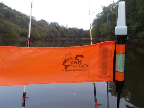 An Orange Flag Is Attached To The Side Of A Boat On Water With Trees In