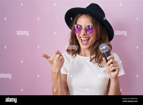 Beautiful Brunette Woman Singing Song Using Microphone Pointing Thumb Up To The Side Smiling