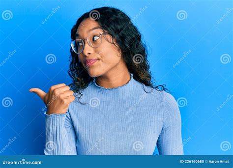 Joven Latina Con Ropa Informal Y Gafas Apuntando El Pulgar Hacia El Costado Sonriendo Feliz Con