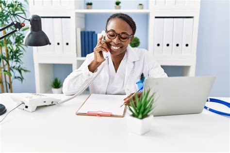 African American Woman Doctor Talking On Telephone Writing On Document