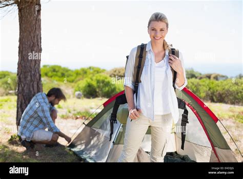 Attractive Blonde Smiling At Camera While Partner Pitches Tent Stock Photo Alamy