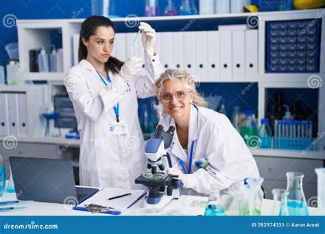 Two Women Scientists Using Microscope Measuring Liquid At Laboratory