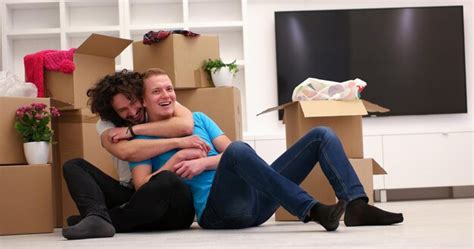Relaxando em casa nova alegre jovem casal gay sentado no chão enquanto caixas de papelão ao