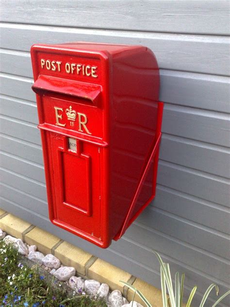 A Red Post Office Mailbox On The Side Of A Building Next To A Flower Bed