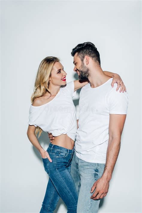 Happy Blonde Woman Standing With Hand In Pocket And Hugging Cheerful Bearded Man On White Stock