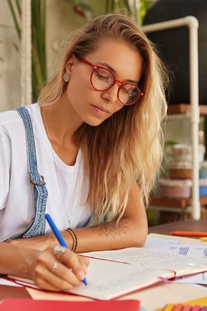 Une étudiante Blonde En Lunettes à Monture Rouge Optique Fait Des Recherches Pour Un Document De