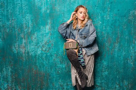 Sexy attraktive stilvolle blonde Frau in Jeans und übergroße Jacke gegen Vintage grüne Wand