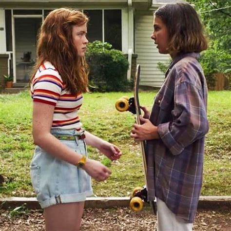 Two People Standing In Front Of A House Talking To Each Other While Holding Skateboards