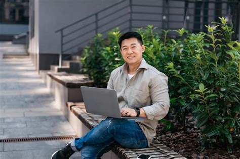 Premium Photo Happy Mature Asian Man Working On Laptop Computer Outdoors Sitting On Bench In