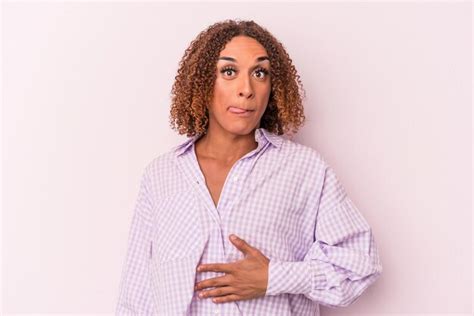 Joven transexual latina aislada de fondo rosa toca la barriga sonríe suavemente come y el