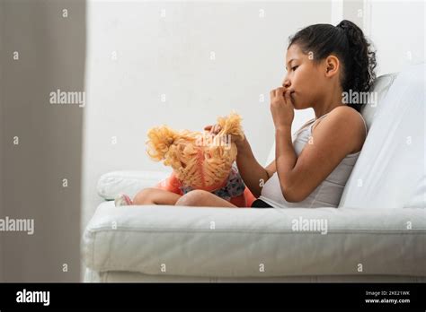 Latina Brunette Girl Sitting Alone On The Sofa While Playing With Her Doll The Girl Is Busy