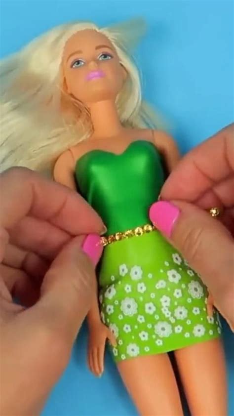 Two Hands Are Holding A Barbie Doll With Blonde Hair And Green Dress