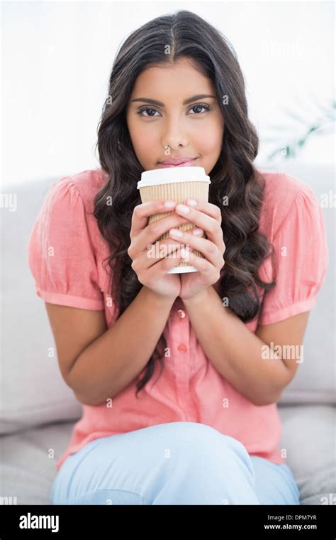 Calm Cute Brunette Sitting On Couch Holding Disposable Cup Stock Photo