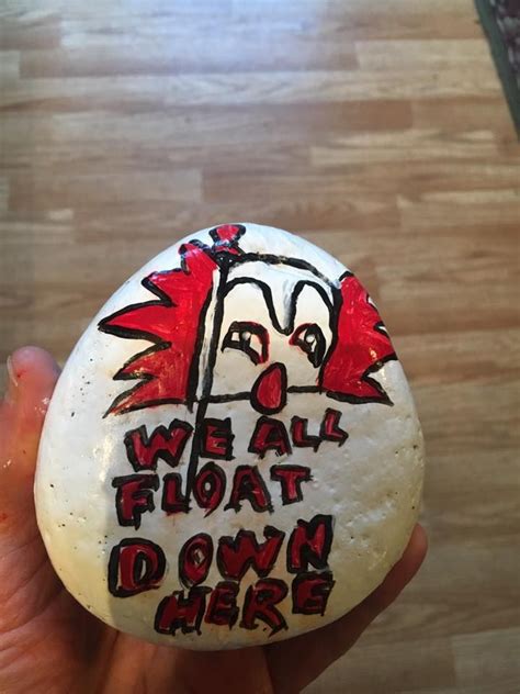 Someone Holding Up A Rock With The Words We All Float Down Here Painted