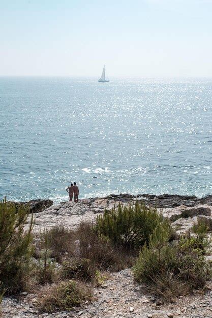 Premium Photo Distant View Of People Naked Standing On Rock By Sea Against Sky