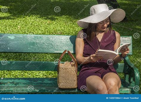 Beautiful Woman Purple Dress Sitting On A Bench And Reading In The