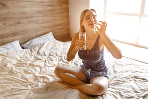 Jeune Belle Femme Blonde Assise Au Lit Le Matin Elle Va Avaler La Capsule Et Boire De L Eau En