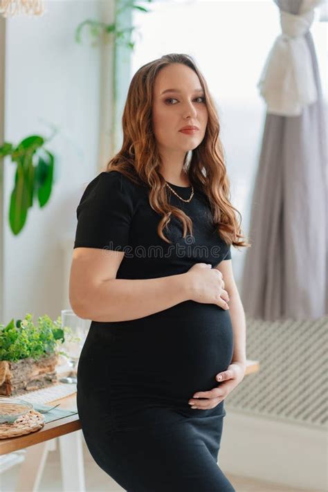 Beautiful Pregnant Woman In Black Dress Touches The Stomach In The Home