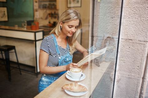 Jeune Femme Blonde Assise Dans Le Caf Et La Lecture Photo Gratuite