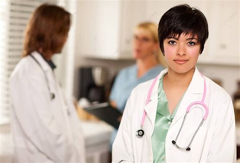 Latina Doctor With A Pleasant Smile Poses For The Camera While Colleagues Converse Photo