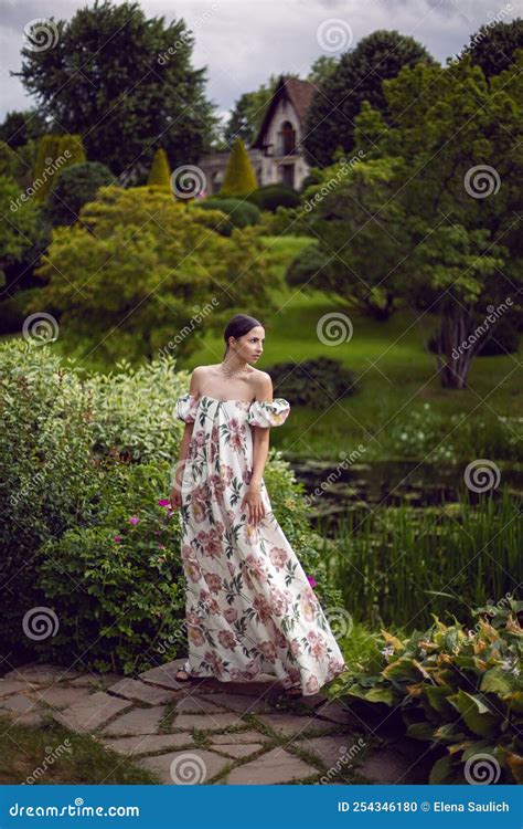 Outdoor Portrait Of A Beautiful Luxury Brunette Woman In A Dress With Flowers Stands Next To The