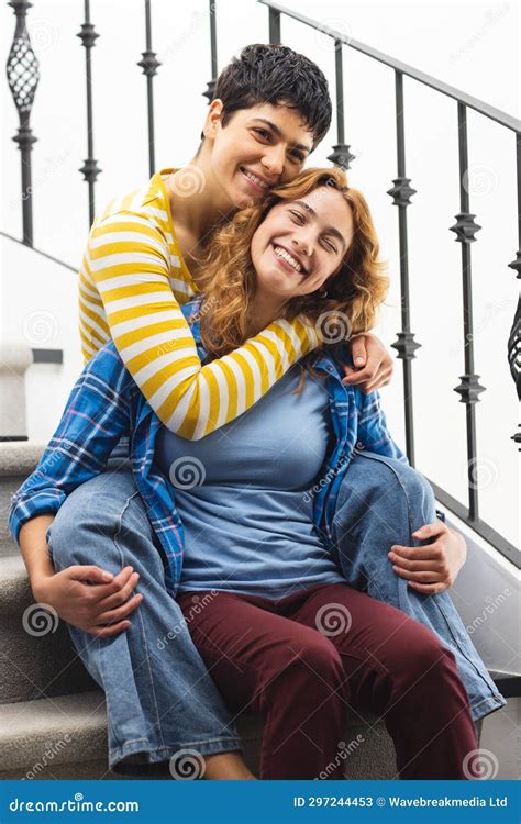 Portrait Of Happy Biracial Lesbian Couple Embracing Sitting On Stairs