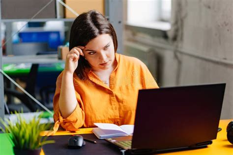 A Brunette Woman In An Orange Blouse Works On A Laptop At Desk In The Office Stock Image Image