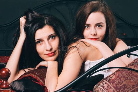 Twee Jonge Vrouwen In Uitstekende Lingerie Op Het Verspreidingsbed Tegen De Zwarte Muur