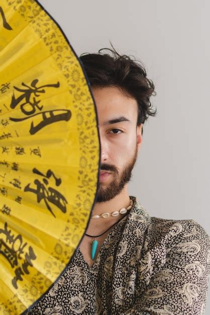 Joven gay latino queer que cubre la mitad de su rostro con un abanico plegable japonés foto
