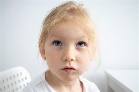 Enfant Fille Blonde Est Assise Sur Une Chaise Blanche à La Table Sur Un Fond Blanc Photo Premium