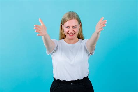 Une Fille Blonde Souriante S étend Et Ouvre Grand Ses Mains à La Caméra Sur Fond Bleu Photo