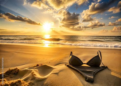 Warm Sunlight Casts A Golden Glow On A Serene Beach Scene Empty Except For A Black Bikini