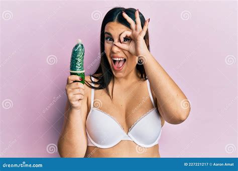 Beautiful Brunette Woman Holding Condom On Cucumber For Sex Education Smiling Happy Doing Ok