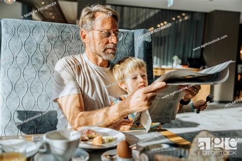 Mature Man With Son Reading Newspaper While Sitting At Table In Hotel Room Stock Photo Picture