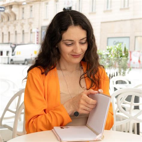 Beautiful 35 Year Old Brunette Woman Sitting In A Cafe And Flipping Through A Diary Notebook