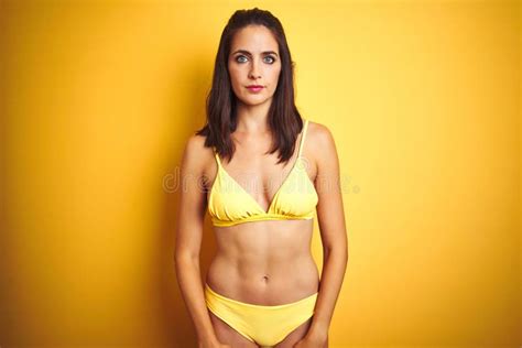 Beautiful Woman Wearing Yellow Bikini On Summer Over Isolated Yellow Background With Serious