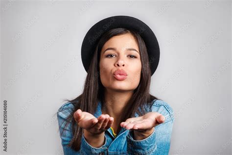 Beautiful Brunette Woman In Black Hat Blowing A Kiss At You Against Gray Background Stock Photo